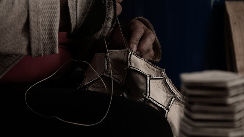A stitcher's hands closing the seam of a Hayworth ball, the cut panels stacked beside her.